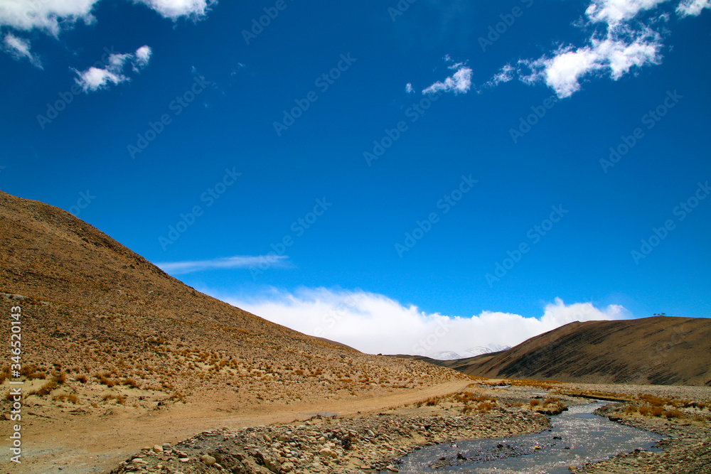 The magnificent scenery of the Everest Scenic Area, the brown hillside, the snowy mountains in the distance, the blue sky and white clouds, the road to the distance