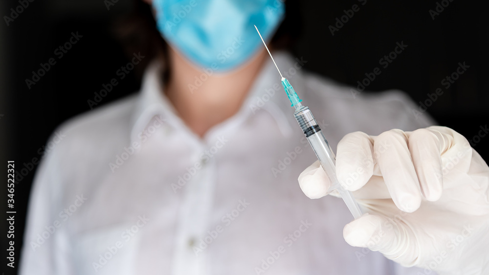 Man in surgical gloves holding medical injection syringe in outstretched hand towards the camera. Selective focus Man in surgical gloves holding medical injection syringe in outstretched hand towards the camera. Selective focus