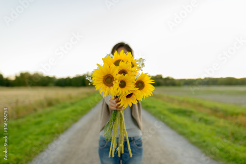 Young woman giving sunflowers against view of the field in nature #346526754