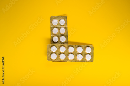 two blister of white pills horizontal and vertical on a yellow background