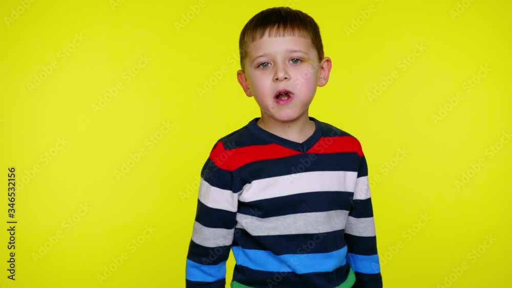 Little child boy in a multi-colored sweater eats chocolate and throws a wrapper at the camera on a yellow background with copy space. Place for text or product. 4K slowmotion footage Little child boy in a multi-colored sweater eats chocolate and throws a wrapper at the camera on a yellow background with copy space. Place for text or product. 4K slowmotion footage