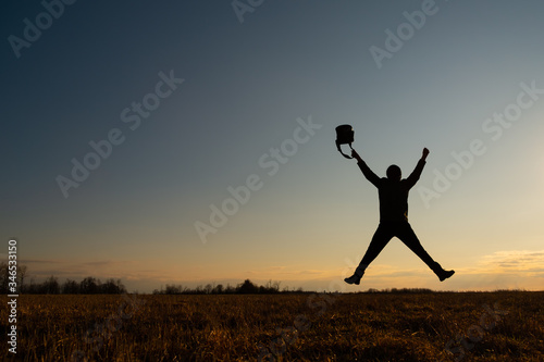 The contour of a man against the sky. The man jumped, stretching his arms and legs in the shape of a star. He has a bag in his hand. Joy concept