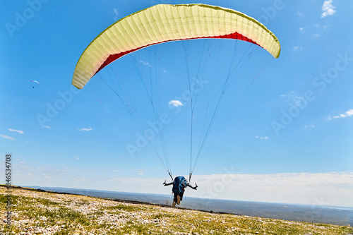 Persona en parapente abierto a punto de saltar desde la colina con cielo azul y nubes de fondo en Cuchi Corral, Cordoba, Argentina, Sudamerica