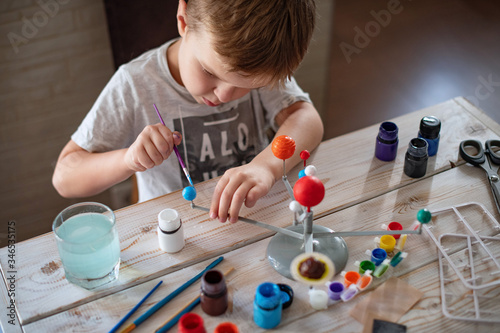 Boy tinkering a model of the solar system Concept of teaching children. Studying astronomy from childhood. Developing creativity from early age. Drawing with brushes and paints. Lockdown entertainment