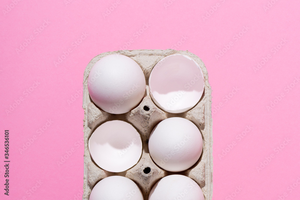 Obraz premium Chicken eggs in a cardboard box on a pink background. Beaten empty eggs, shell. Highlight the concept of the crowd.