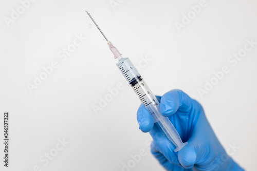 Healthcare cure concept with a hand in blue medical gloves holding Coronavirus vaccine in syringe.