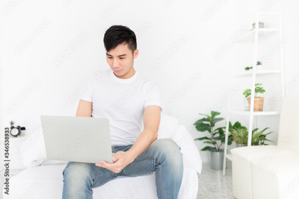 asian man relax in bedroom, he play internet and search information with laptop, he feeling happy and smile, work from home asian man relax in bedroom, he play internet and search information with laptop, he feeling happy and smile, work from home