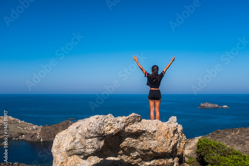 Rear view of a girl admiring a view of the scenic landscape of the Mediterranea Sea at Cap de Creus, Catalonia, Spain.