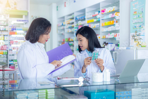 Two Asian pharmacists check medicine list in drugstore. Medicine, pharmaceutics, healthcare and people concept.