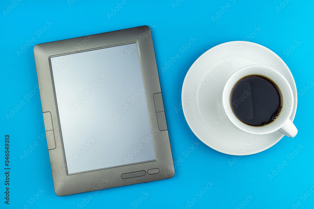 a coffee Cup on a saucer and an e-book on a blue background. a coffee Cup on a saucer and an e-book on a blue background.