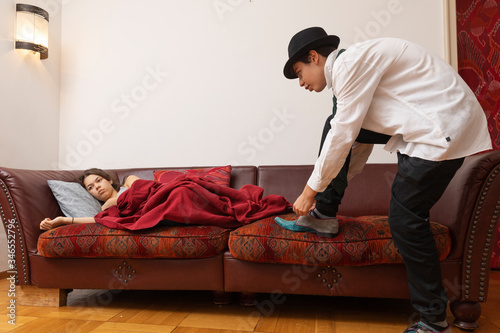 Businessman fastens his shoes while the girl is lying on the sofa with a blanket