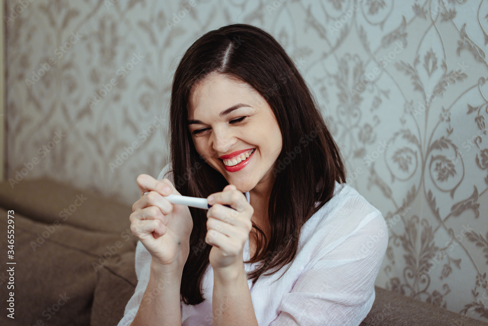Young woman rejoices while looking at a positive pregnancy test Young woman rejoices while looking at a positive pregnancy test