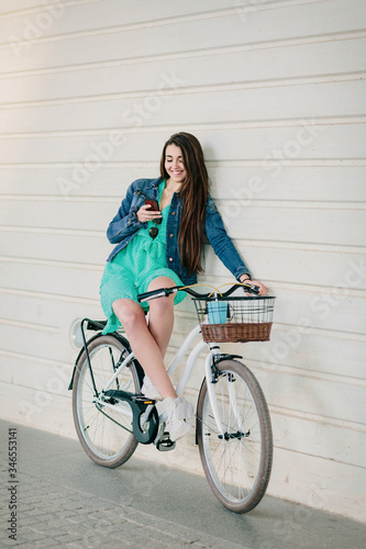 Young girl consulting her smartphone while waiting sitting on her bike on the street