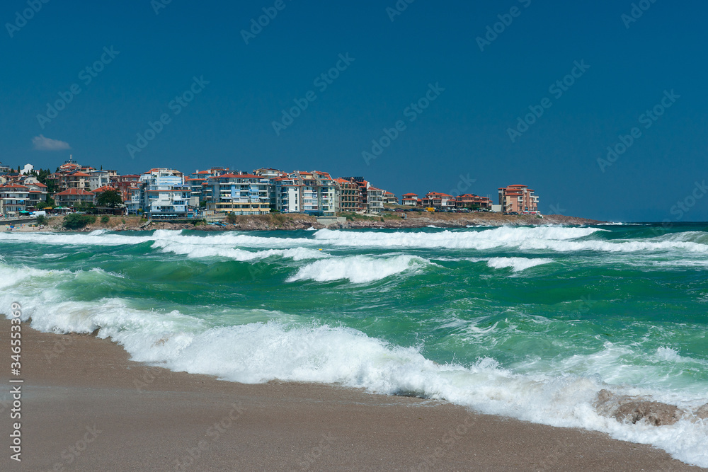 The beach in the city of Sozopol in Bulgaria a beautiful turquoise sea is storming, waves are running on the sand, against the background of the city