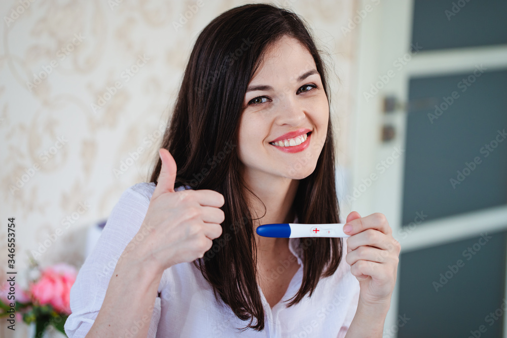 Young woman rejoices while looking at a positive pregnancy test Young woman rejoices while looking at a positive pregnancy test