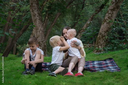 Happy family of four having picnic at the park. Mother and three children sitting on picnic blanket. Weekend outdoors