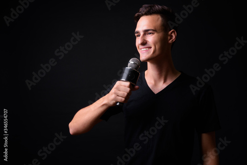 Portrait of happy young handsome man thinking while using microphone © Ranta Images