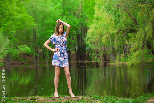 Portrait of a young beautiful woman in blue dress posing by the lake