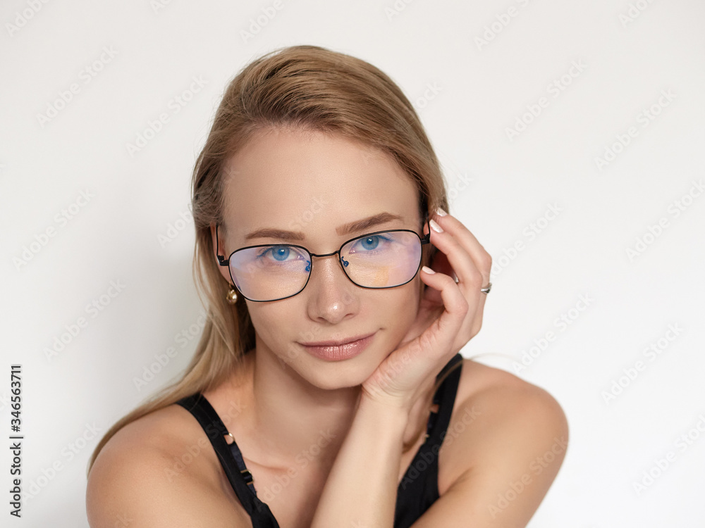 Headshot portrait of a cute natural looking blonde woman wearing simple black blouse and nerd glasses posing on a white background resting chin on hand