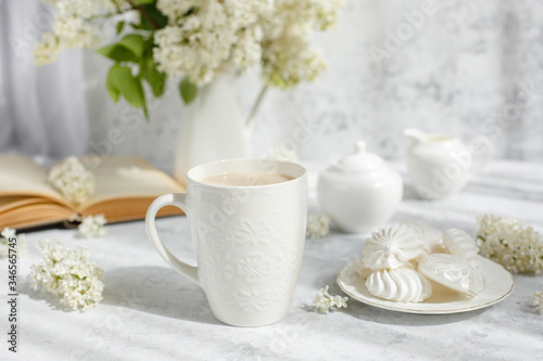 Still life vase with a bouquet of white lilac  a Cup of coffee with marshmallows  a plate of meringue  a sugar bowl and a milk jug   an old book. Postcard good morning.