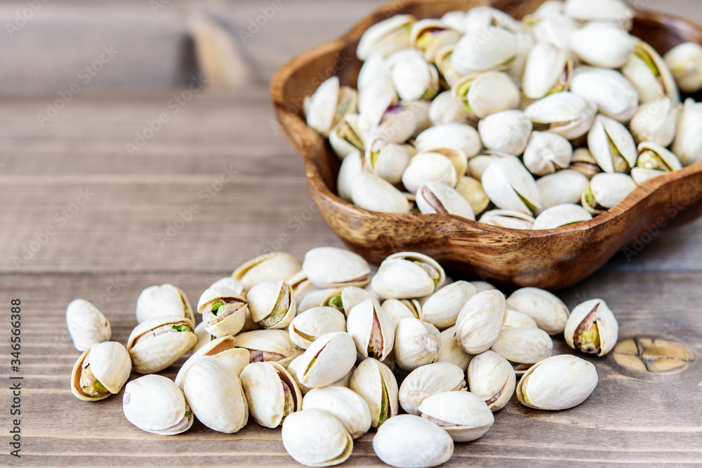 Heap of pistachios in the wooden bowl and on the wooden kitchen table closeup. Healthy food concept. Heap of pistachios in the wooden bowl and on the wooden kitchen table closeup. Healthy food concept.