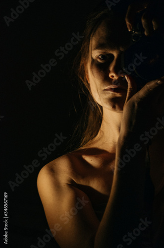 Half face portrait of a young woman in low key holding a camera