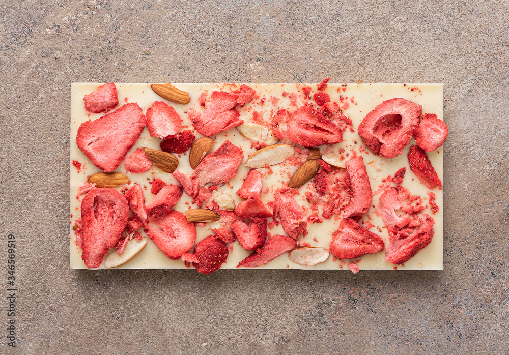 A bar of white chocolate with fried almonds and freeze-dried strawberries on a light background. Top view, flat lay.