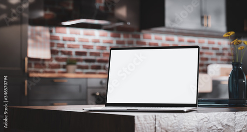 Laptop with a blank screen on a wooden table on the background of a loft kitchen