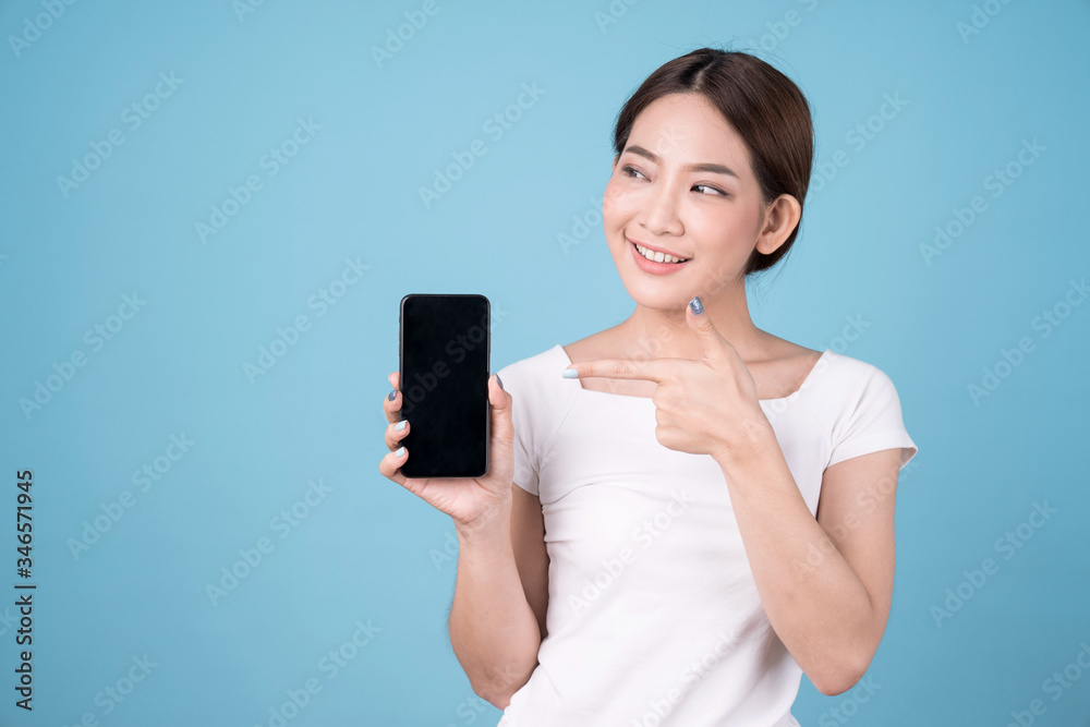 Portrait of a cute Asian girl pointing a finger on an empty mobile screen, Isolated over blue background. Portrait of a cute Asian girl pointing a finger on an empty mobile screen, Isolated over blue background.