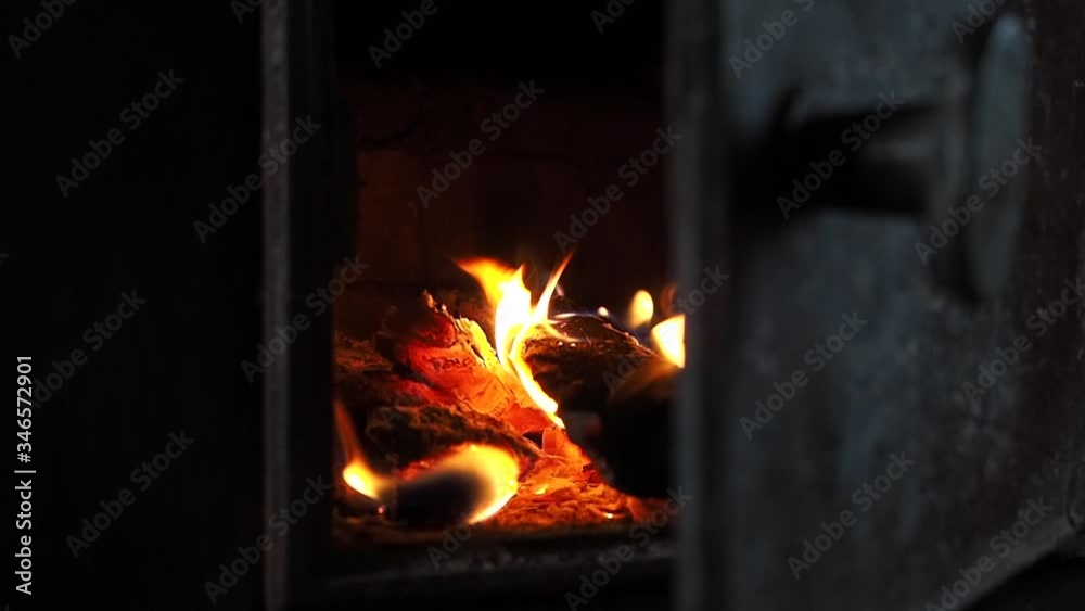 Wood burning in a cast-iron stove, close-up. Heating a country house with a stove. Bright flames burst out through the open door of the furnace. The concept of warming up in winter by the fireplace.