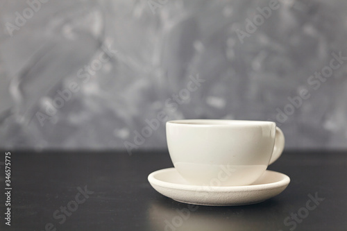 A white cup on the black table. On gray background
