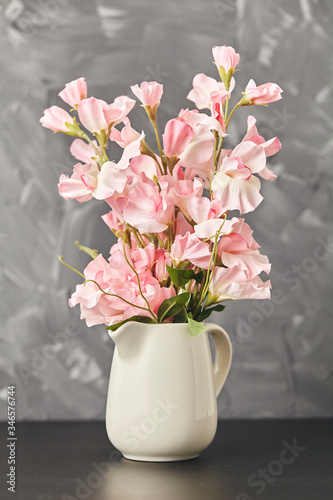 Pink flower in vase on black table on gray background. Close up