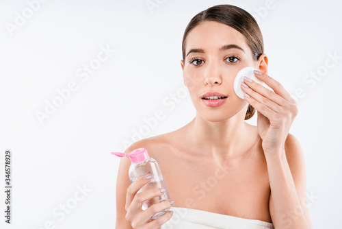Attractive half naked woman using facial lotion with cotton pad isolated over white background