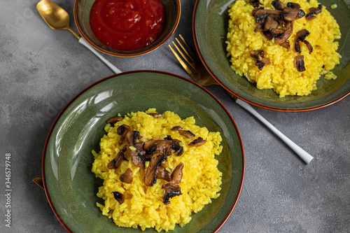Italian risotto with champignons and parmesan on a gray background in dark plates. Rice is seasoned with turmeric and herbs.