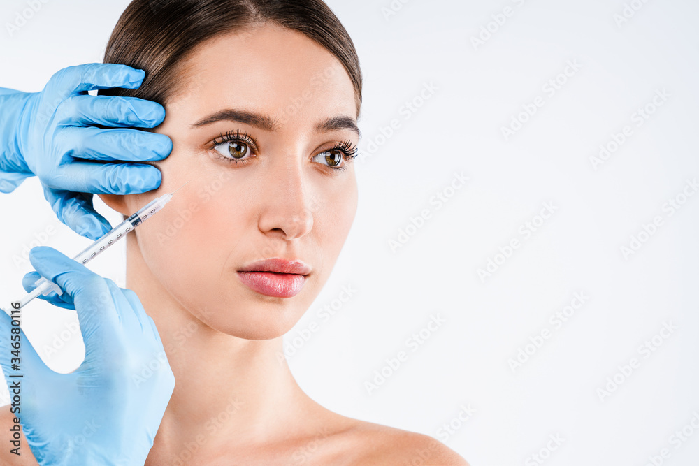 Beautiful young woman gets beauty injection in eye area from sergeant isolated over white background.