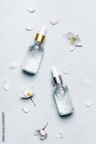 Cosmetic liquid gel products and white flowers on blue background. Beauty skin care concept