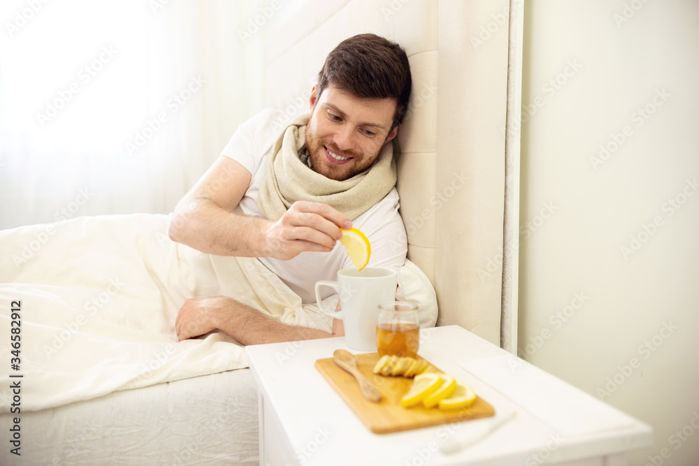Sick Man in Bed Adding Lemon into Tee Smilling. Man Ill in Bed Self Healing. Self Treatment at Home. Man Drinking Hot Tea in Bed. Sick Man in Bed Adding Lemon into Tee Smilling. Man Ill in Bed Self Healing. Self Treatment at Home. Man Drinking Hot Tea in Bed.