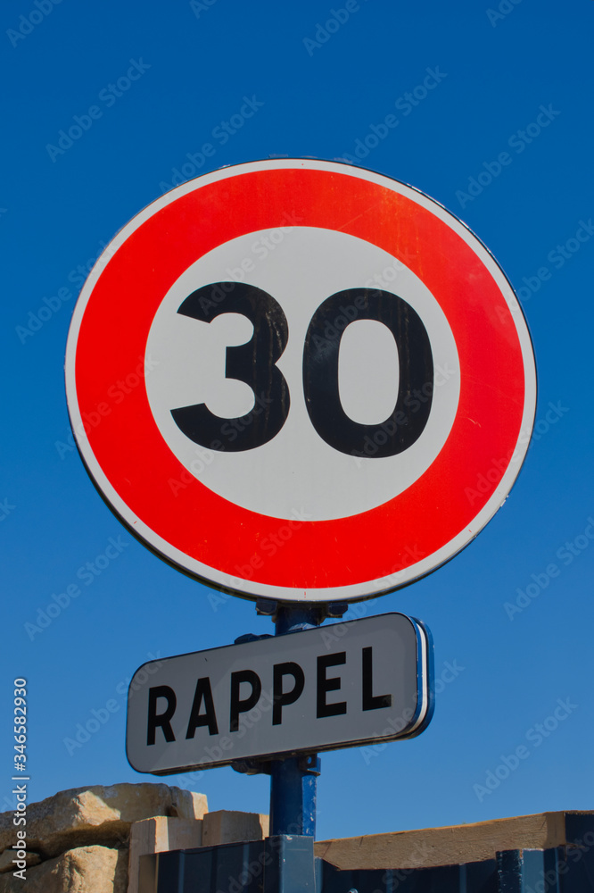 traffic sign with a speed limit of 30 and the French word for remember against blue sky traffic sign with a speed limit of 30 and the French word for remember against blue sky