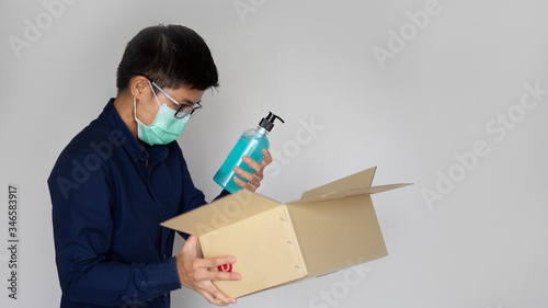 Delivery man employee wearing face mask gloves holding package paper box. He open and looking alcohal gel. Service quarantine pandemic coronavirus virus 2019-ncov concept
 photo