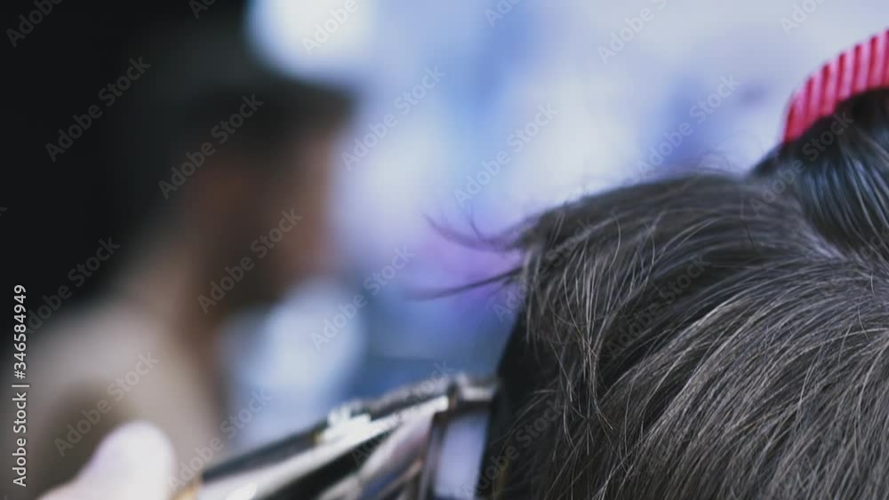 CU, slow motion: male hairdresser does trendy haircut to young customer with black hair using modern shiny golden machine in salon extreme closeup
