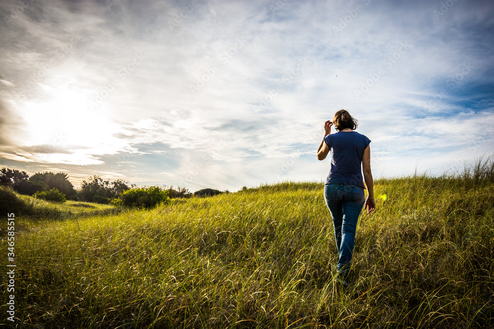 Joven mujer caminando en el pasto al atardecer Joven mujer caminando en el pasto al atardecer