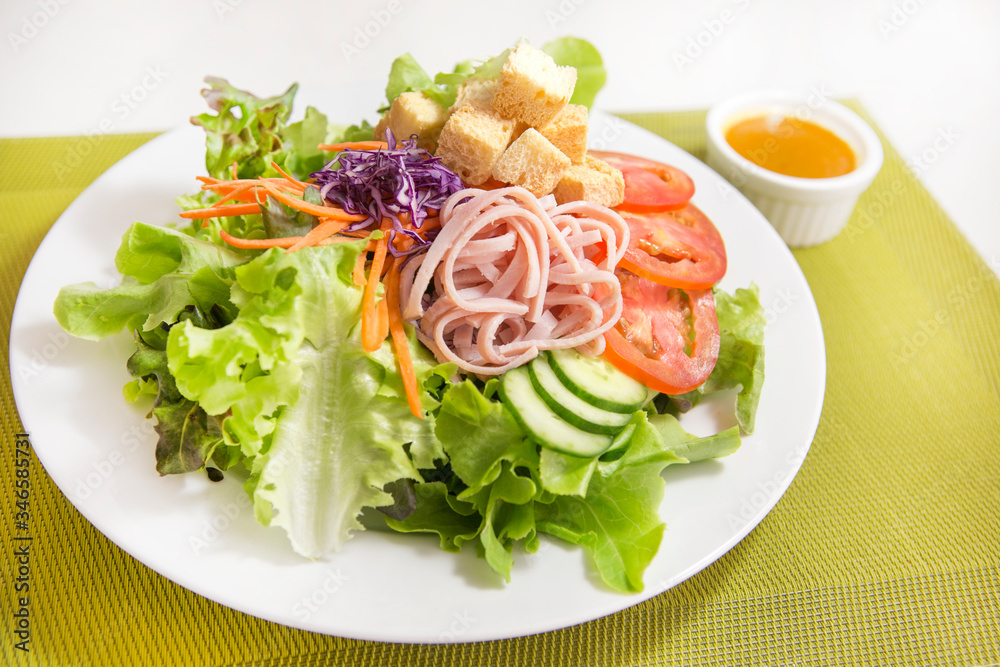 vegetable salad top with ham strips and crouton in white plate serve with dressing sauce on a green placemat vegetable salad top with ham strips and crouton in white plate serve with dressing sauce on a green placemat