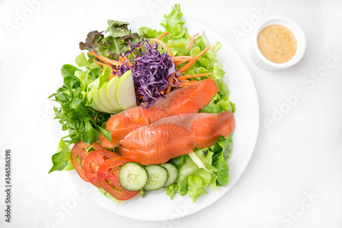 vegetable salad top with smoked salmon and sliced green apple on a white plate isolated white background