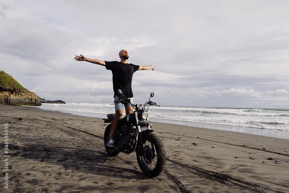 Fototapeta premium young man spread his arms on a motorcycle. ocean coast. freedom.