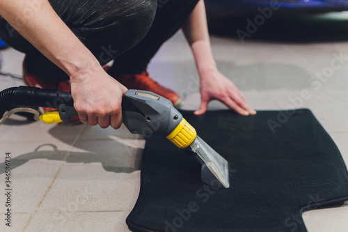 Obraz na plátně Dry cleaning of black mats for cars, vacuum cleaner removes dirt, pink rubber gloves, car washing