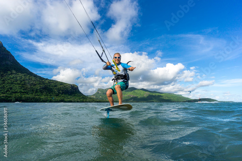 professional kiter t rides by hydrofoil on a beautiful background of mountain, spray and beautiful clouds of Mauritius