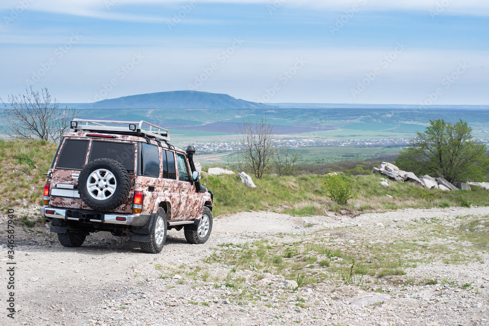 Off-road vehicle rides on mountainous terrain. View of the valley and mountains. A wonderful spacious place for a trip. Modern jeep with an unusual painting. Car tourism in Russia.
