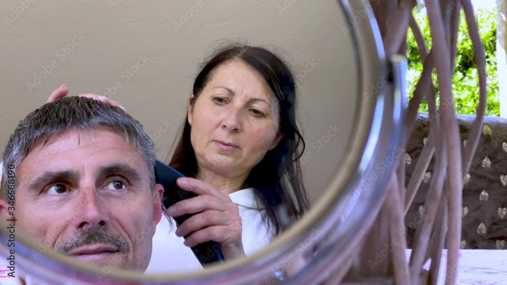 Haircut at home. Female hairdresser combing hair to her husband with mrror reflections Haircut at home. Female hairdresser combing hair to her husband with mrror reflections