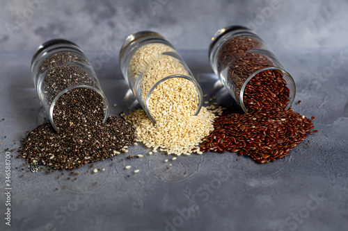 Chia, flax and sesame seeds in a glass bowl contain healthy vitamins and minerals. On a gray background under concrete.