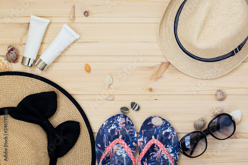 beach accessories: men's and women's straw hats, sunglasses, flip-flops and two white tubes of sunscreen on a wooden background